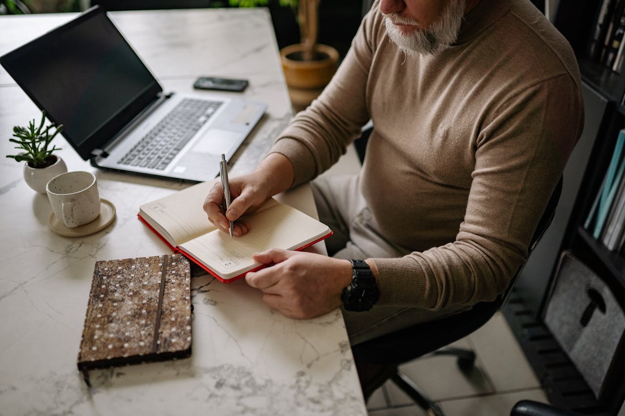Man writing in a notebook at a desk during a self-guided midlife reflection and reset