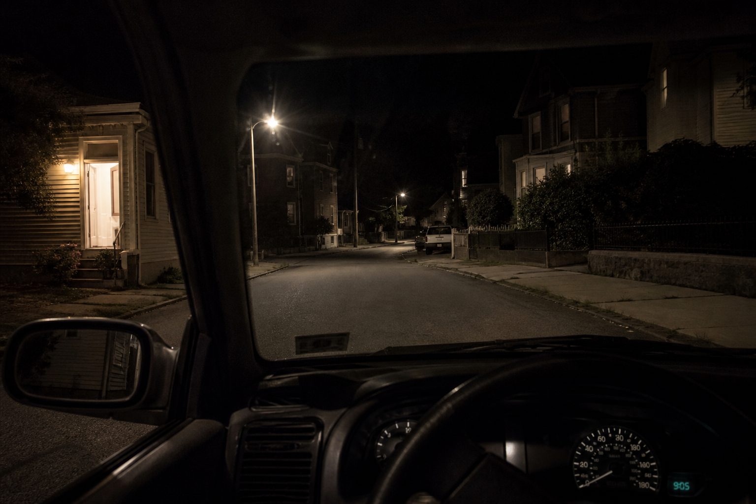 Dark residential side street seen from inside a parked car